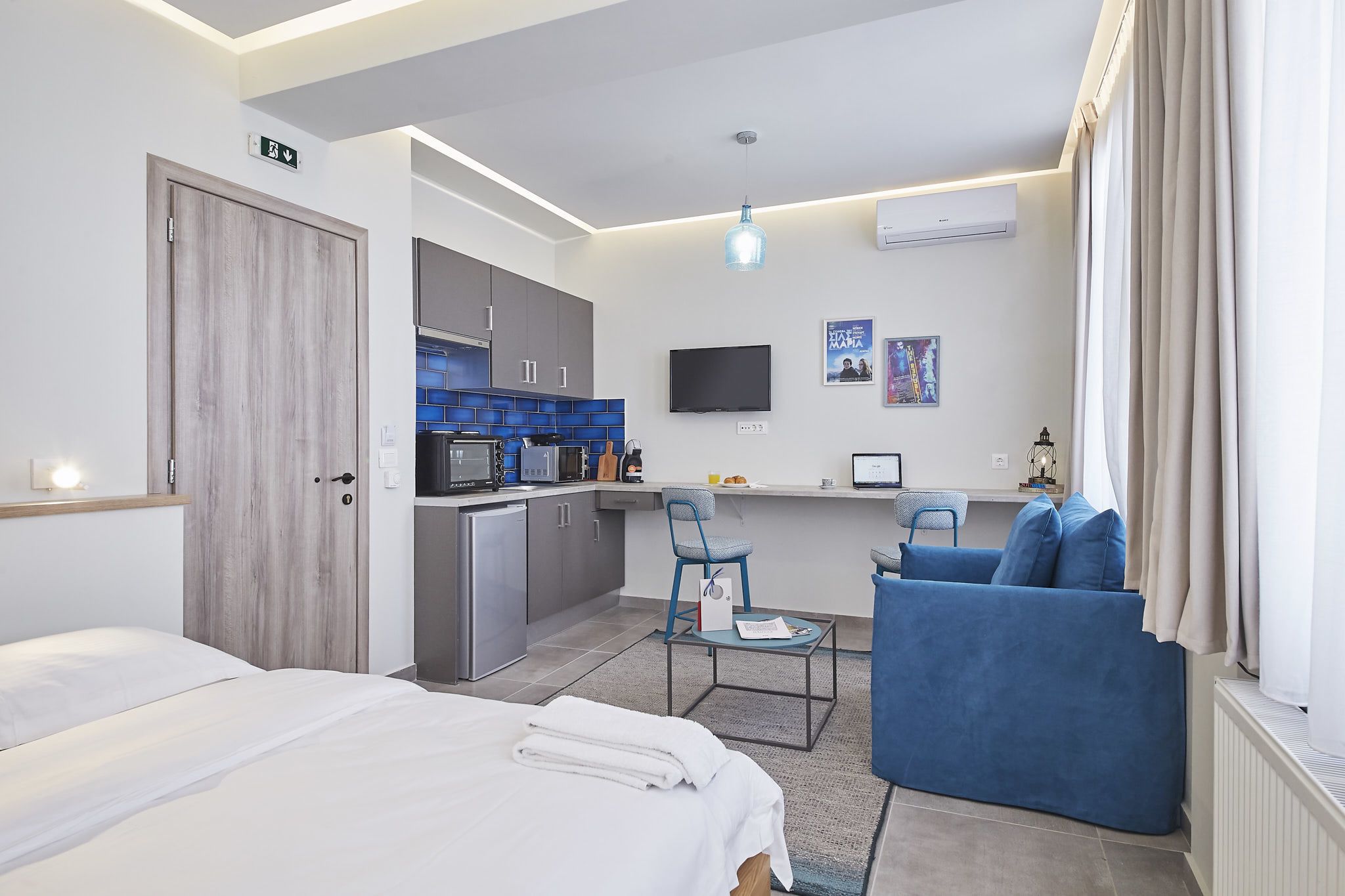 Ein modernes Hotelzimmer mit Bett, Schreibtisch, Küchenzeile und einer Sitzecke.