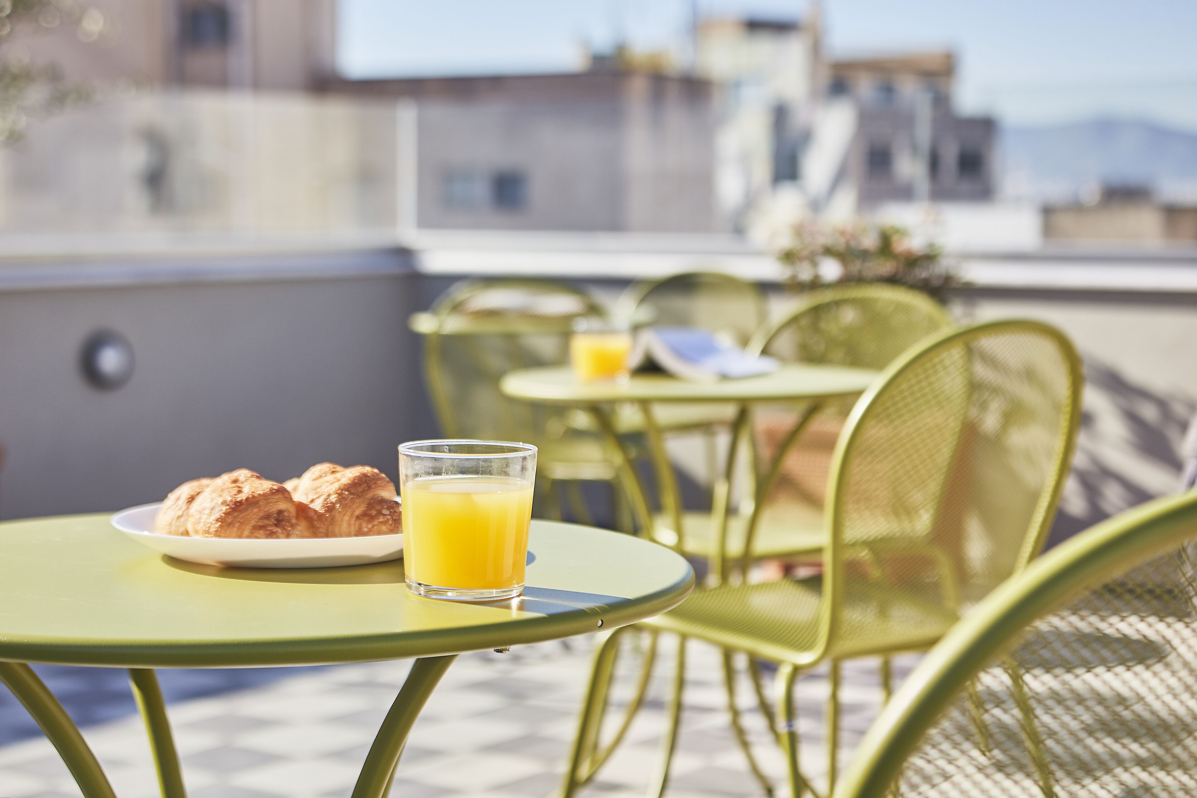 A rooftop terrace with outdoor seating, a plate of croissants, and a glass of orange juice.