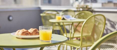 A rooftop terrace with outdoor seating, a plate of croissants, and a glass of orange juice.
