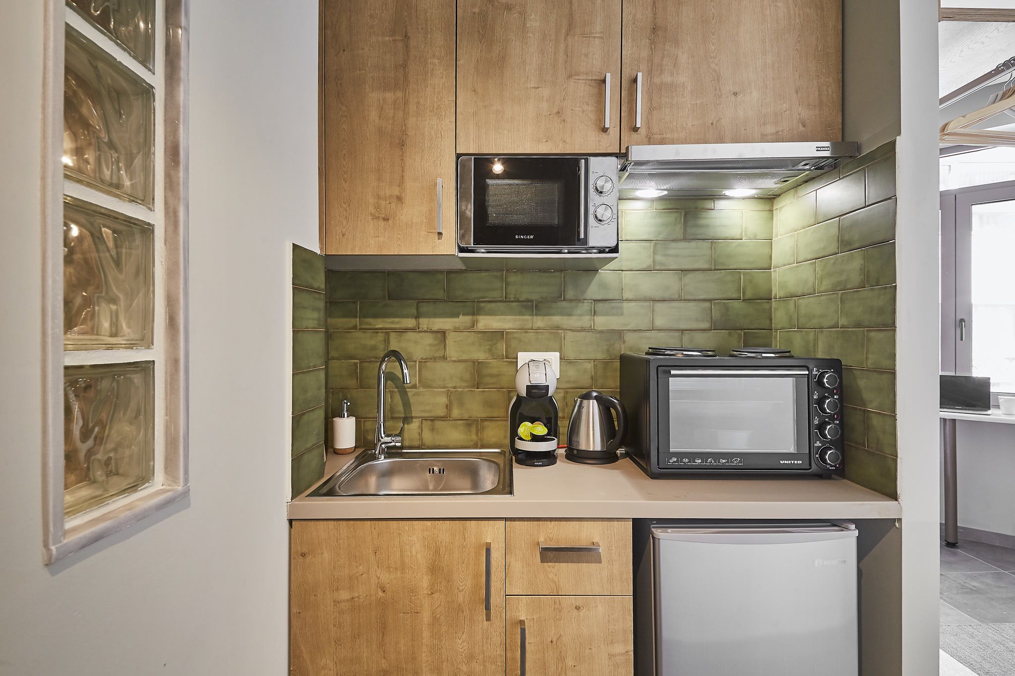 A compact kitchen with wooden cabinets, a microwave, a toaster, a coffee maker, and a refrigerator.