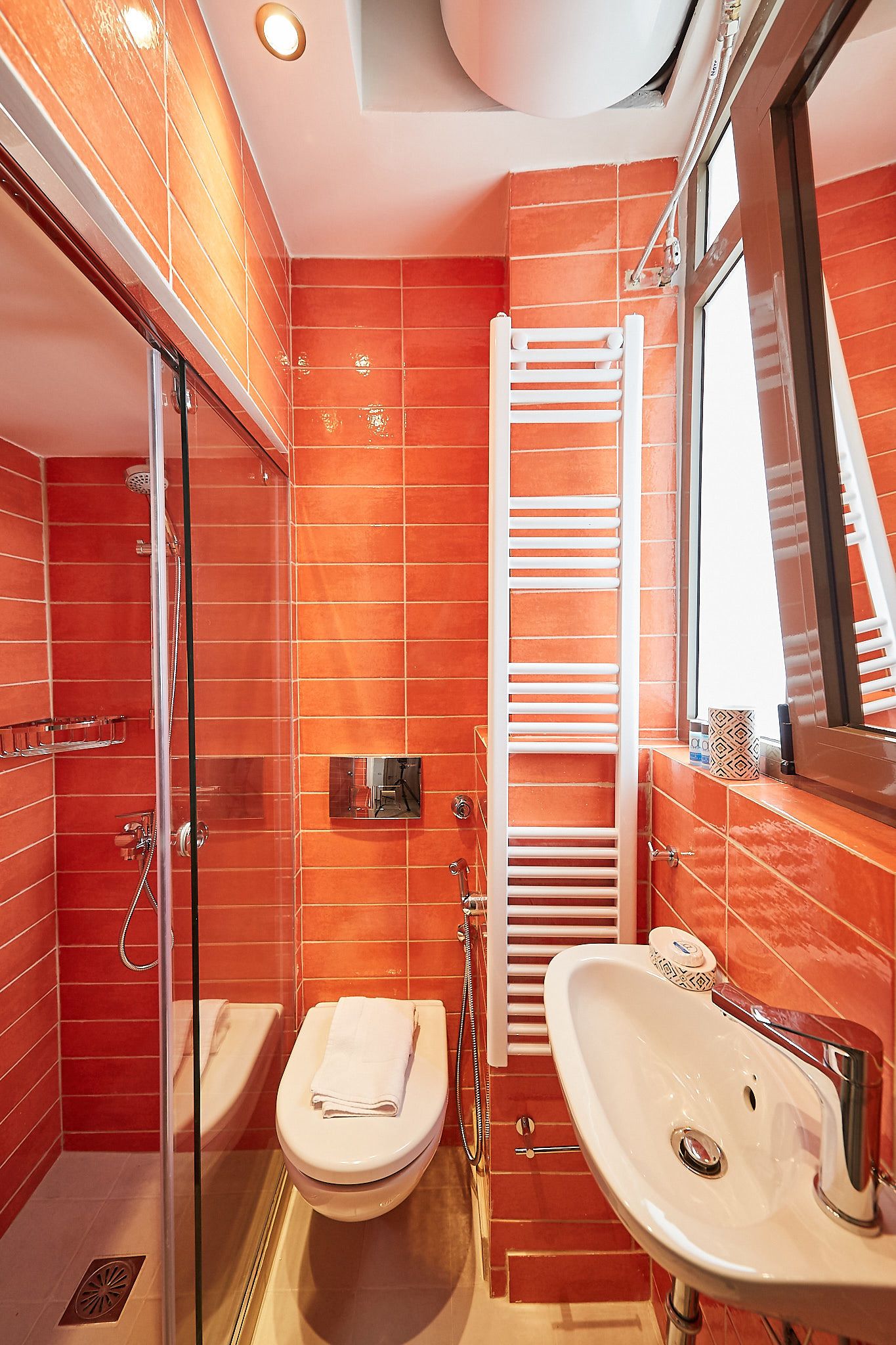 A bathroom with red tiles, a glass shower enclosure, a white toilet, and a sink with a mirror.