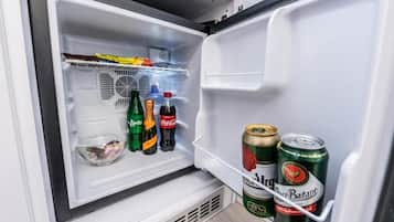 Un refrigerador abierto con estantes que contienen bebidas y un recipiente de plástico transparente.
