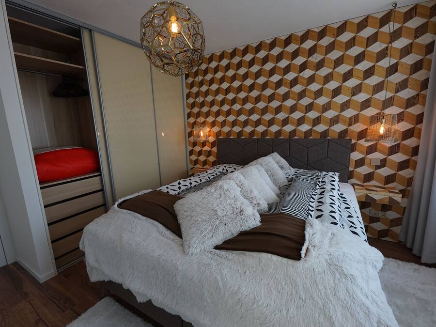 A bedroom with a bed, a wardrobe, and a geometric-patterned wall.