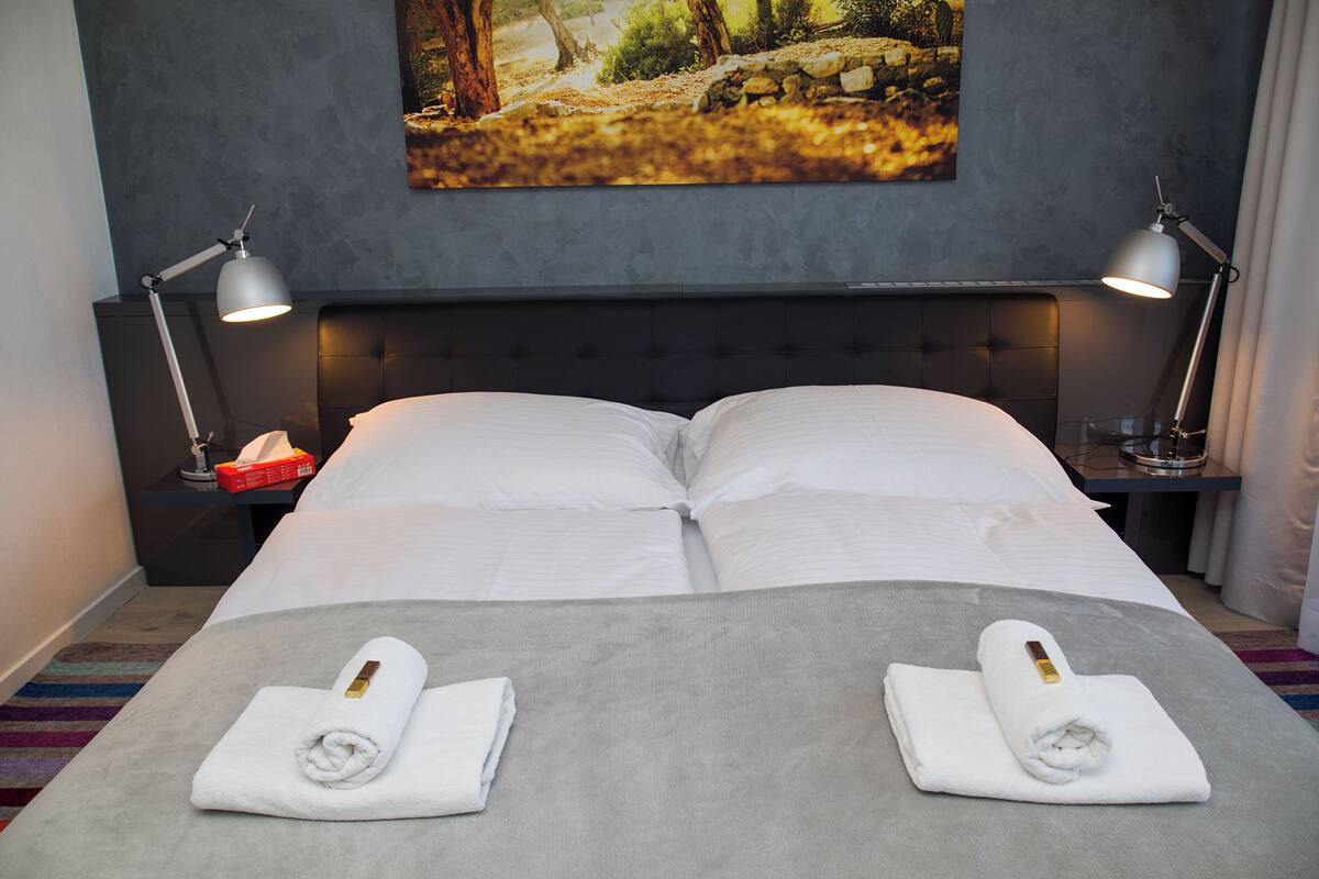 A hotel room with a large bed, two bedside tables with lamps, a painting on the wall, and two towels on the bed.