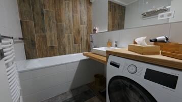 Un baño moderno con una bañera blanca, una lavadora Bosch y un mueble de tocador de madera.