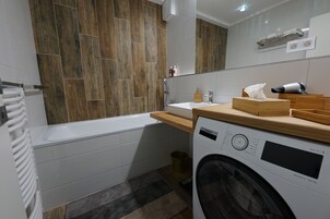 Un baño moderno con una bañera blanca, una lavadora Bosch y un mueble de tocador de madera.