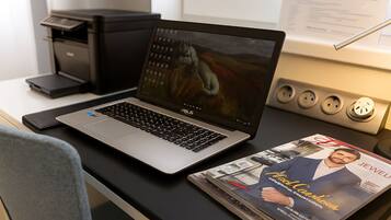 Un laptop su una scrivania, con una rivista che mostra un uomo in abito.