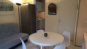 A compact living space with a kitchenette, a dining area with a round table and chairs, and a grey sofa. - little house by the sea (Piriac-sur-Mer)
