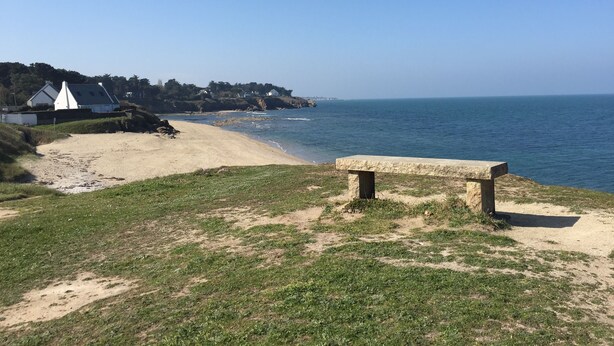 A beach with a stone bench, grassy area, and a view of the sea. - little house by the sea (Piriac-sur-Mer)