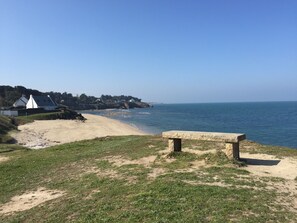Een strand met een stenen bank, een grasveld en uitzicht op zee.