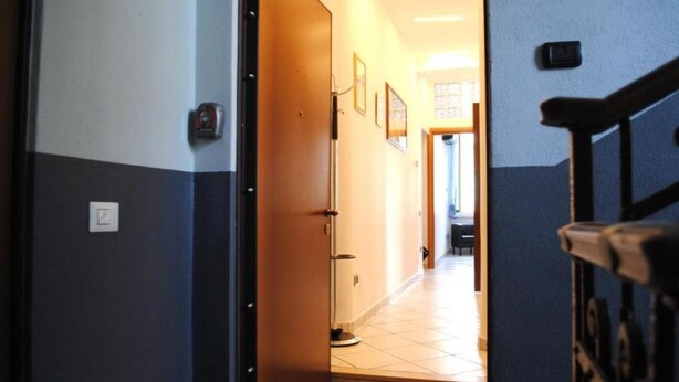 A hallway with a door leading to a room. There are framed pictures on the wall, a light switch, and a thermostat. - BNBOOK BORROMEO 1 RHO (RHO)