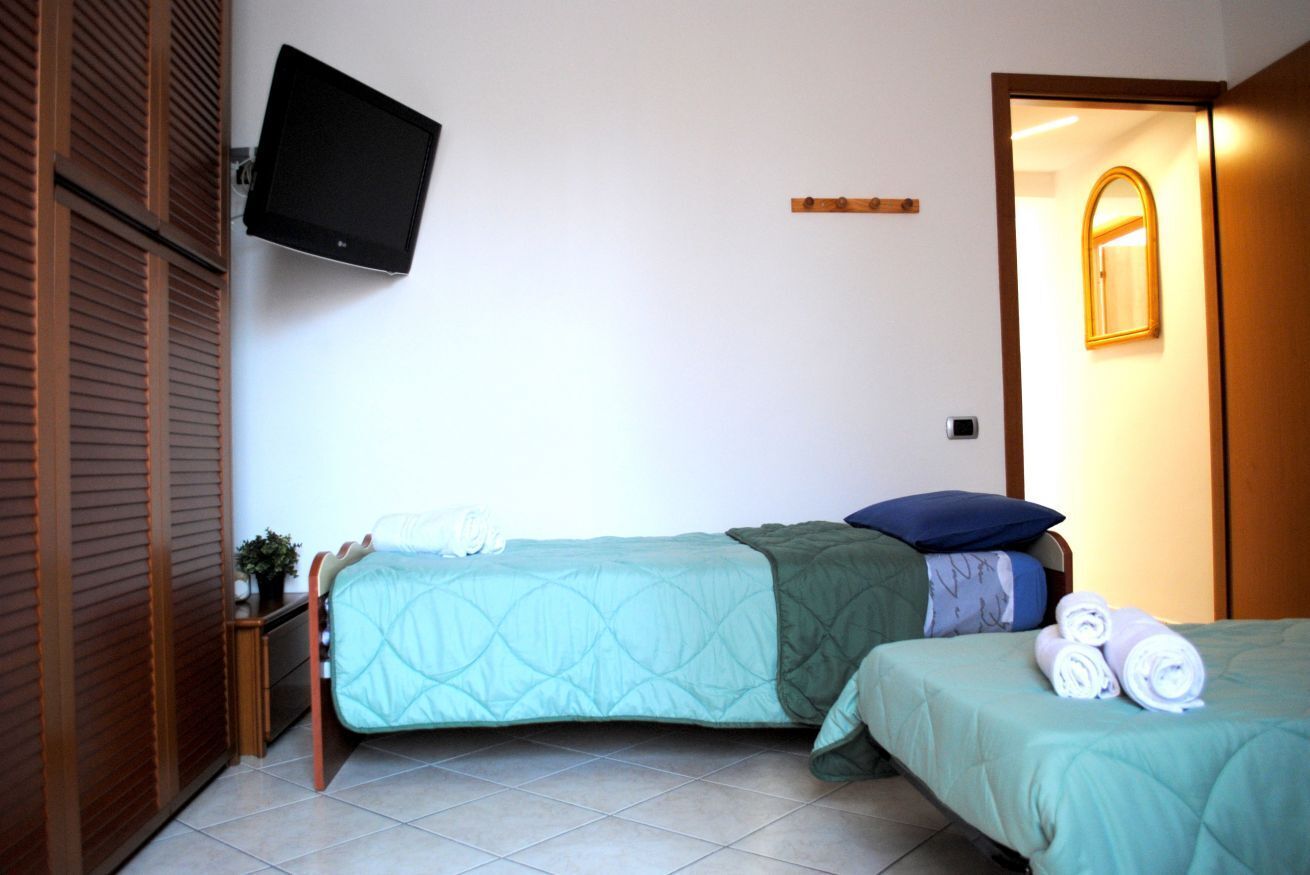 A room with two beds, a television mounted on the wall, a wooden wardrobe, and a mirror on the door.