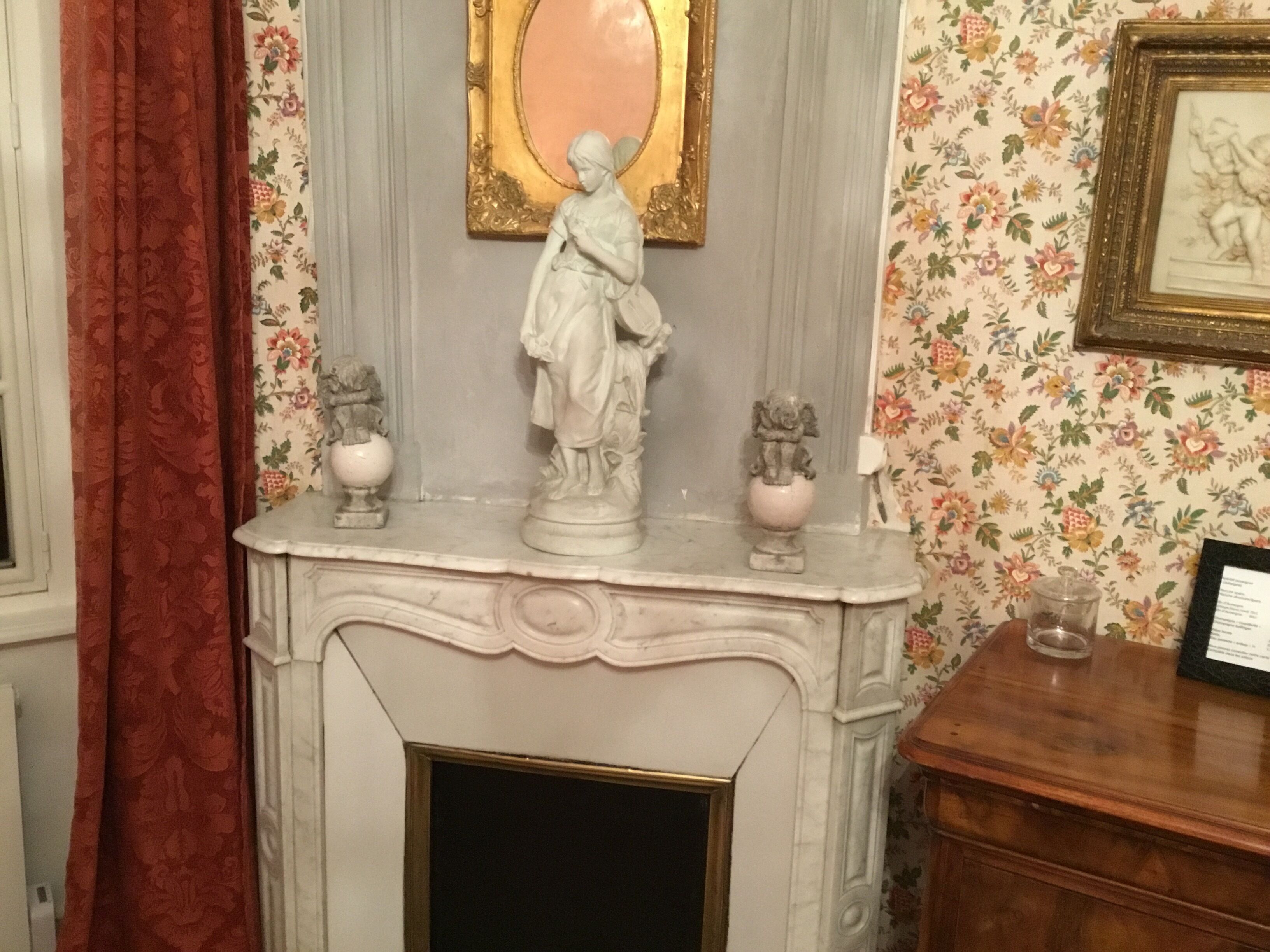 A fireplace with a white mantel, flanked by two statues, and a framed picture above it.
