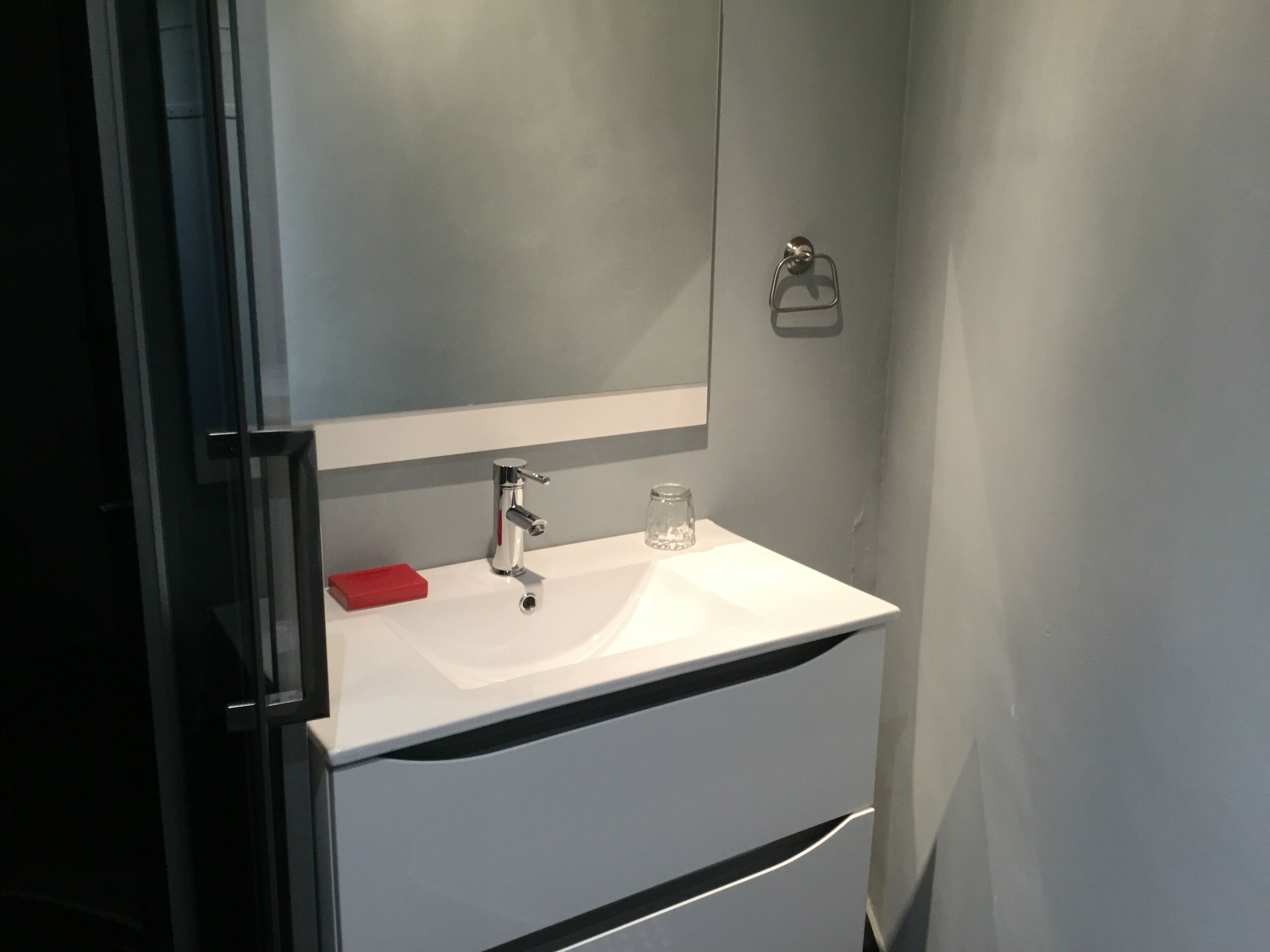 A bathroom with a white sink, a mirror, and a red soap dish.