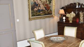 A dining table with chairs, a decorative tray, a painting on the wall, and a wooden cabinet with a lamp and flowers.