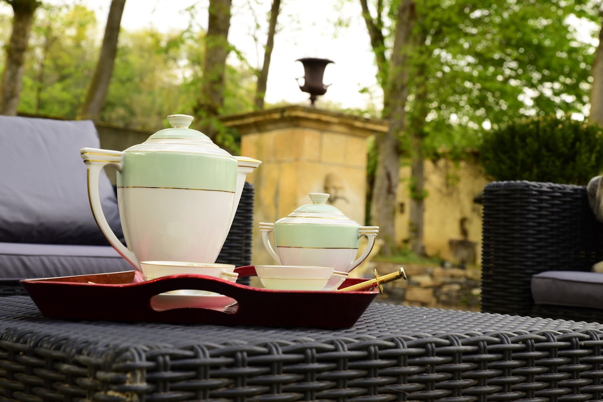 Una mesa de mimbre con una bandeja que contiene un hervidor de agua, tazas y un juego de té.