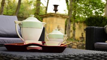 Una mesa de mimbre con una bandeja que contiene un hervidor de agua, tazas y un juego de té.