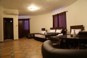 A hotel room with two beds, a dining table, and an air conditioning unit.