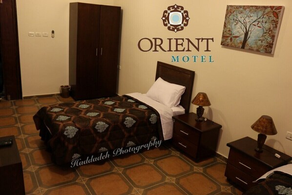 A hotel room with a bed, nightstands, a wardrobe, and a wall-mounted sign for Orient Motel.