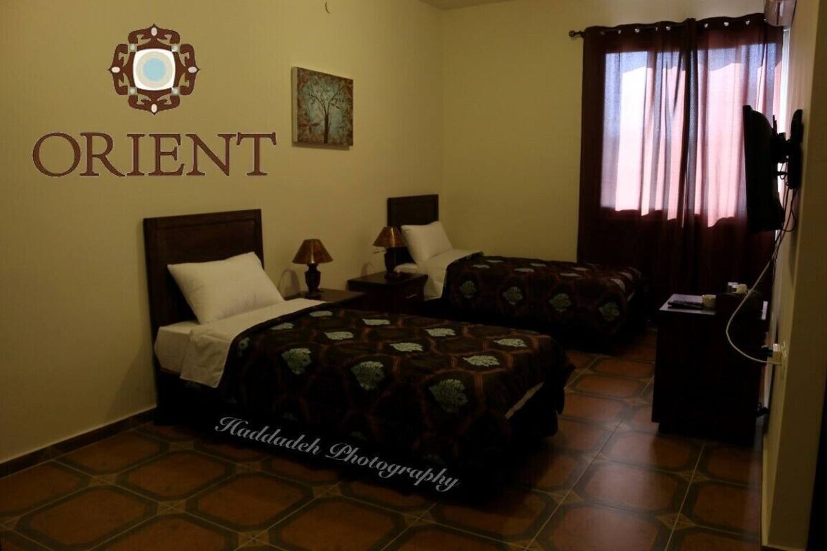 A hotel room with two beds, a nightstand, a lamp, a painting, and a curtain.