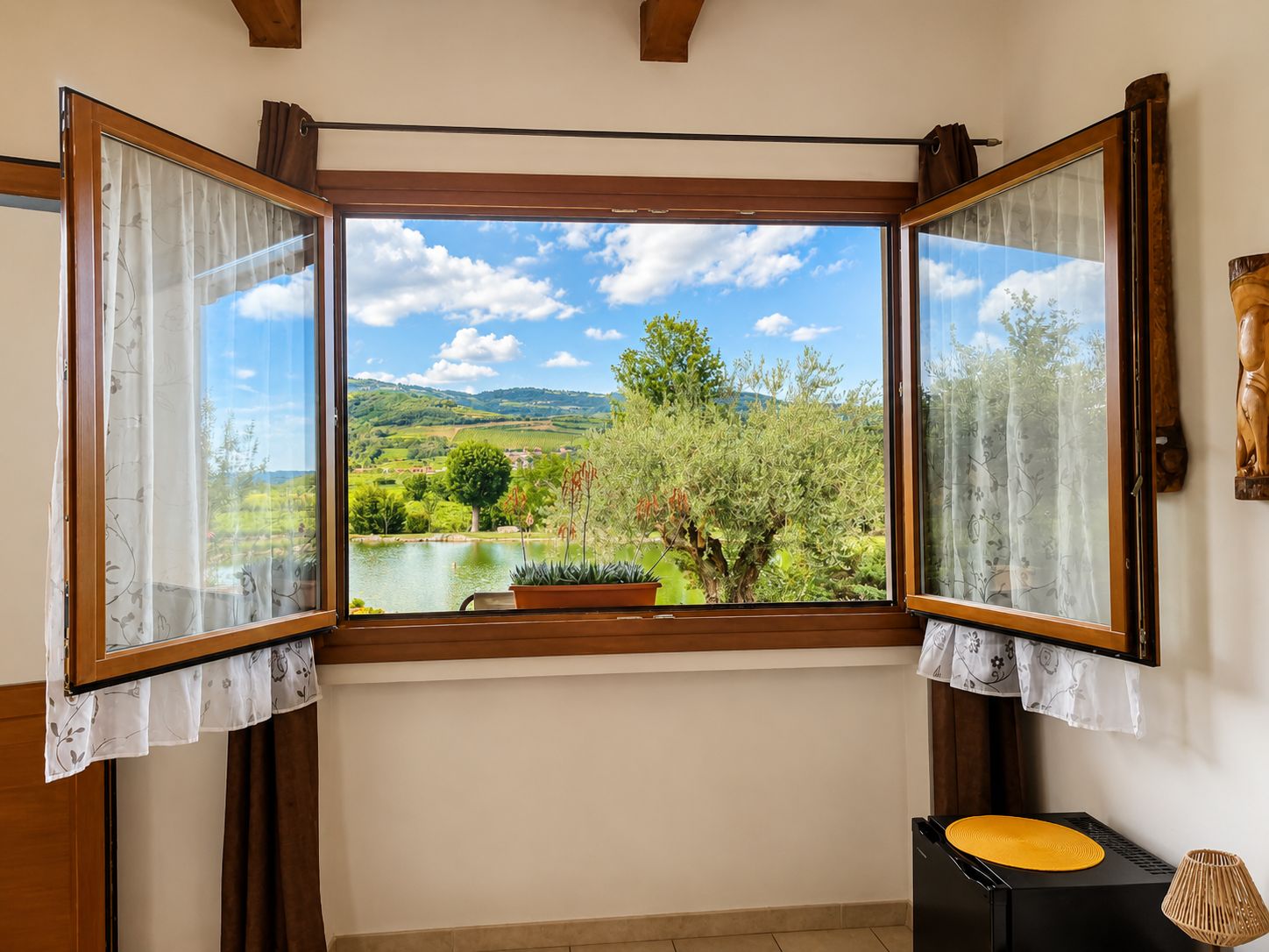 Quarto com grande janela que oferece vista para um lago, árvores e colinas.
