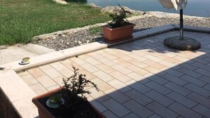 Une terrasse avec vue sur un lac, un parasol blanc et des plantes en pot.