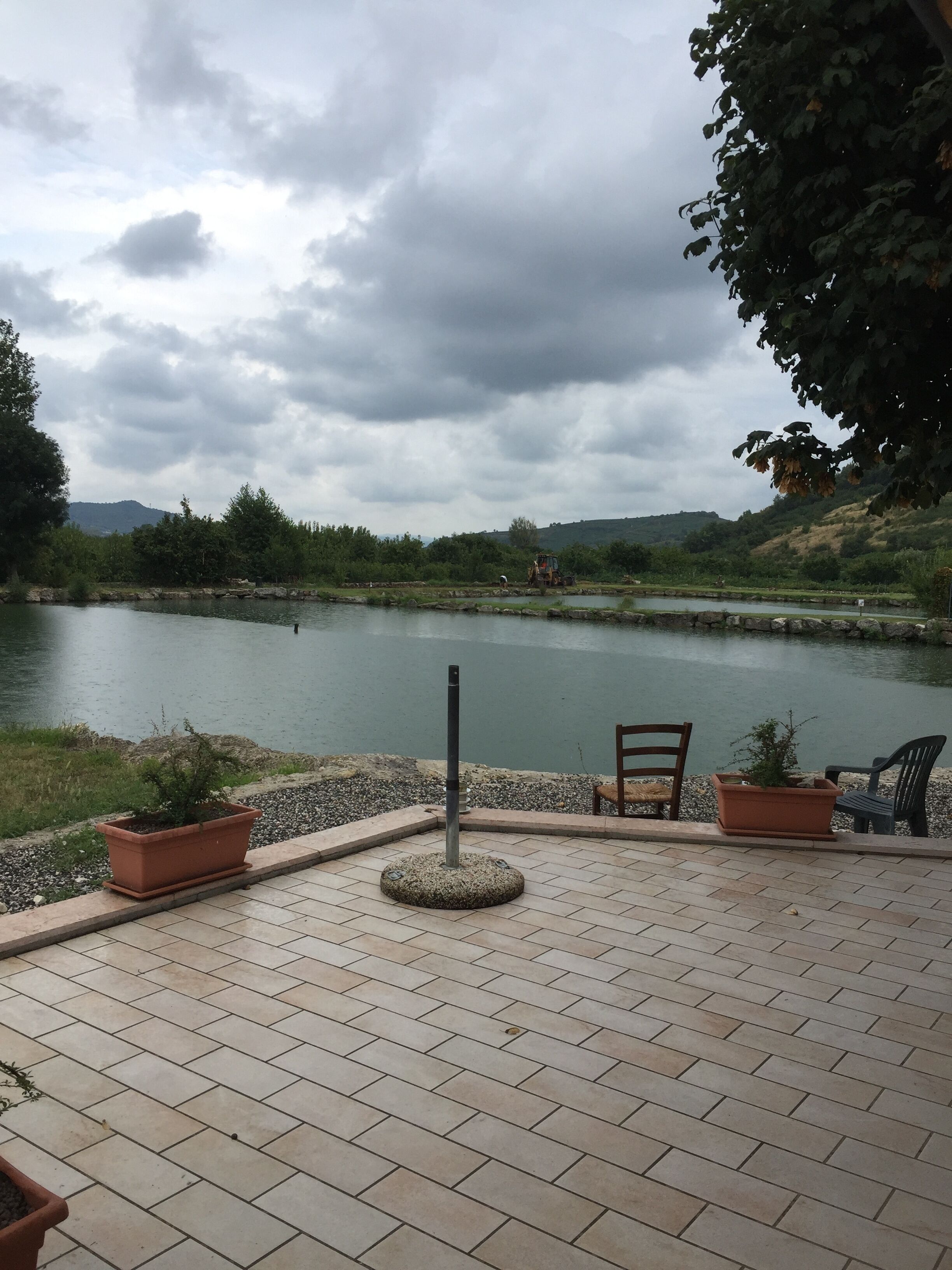 Une terrasse dallée agrémentée de plantes en pot, d’une chaise et offrant une vue sur un lac avec des montagnes en arrière-plan.