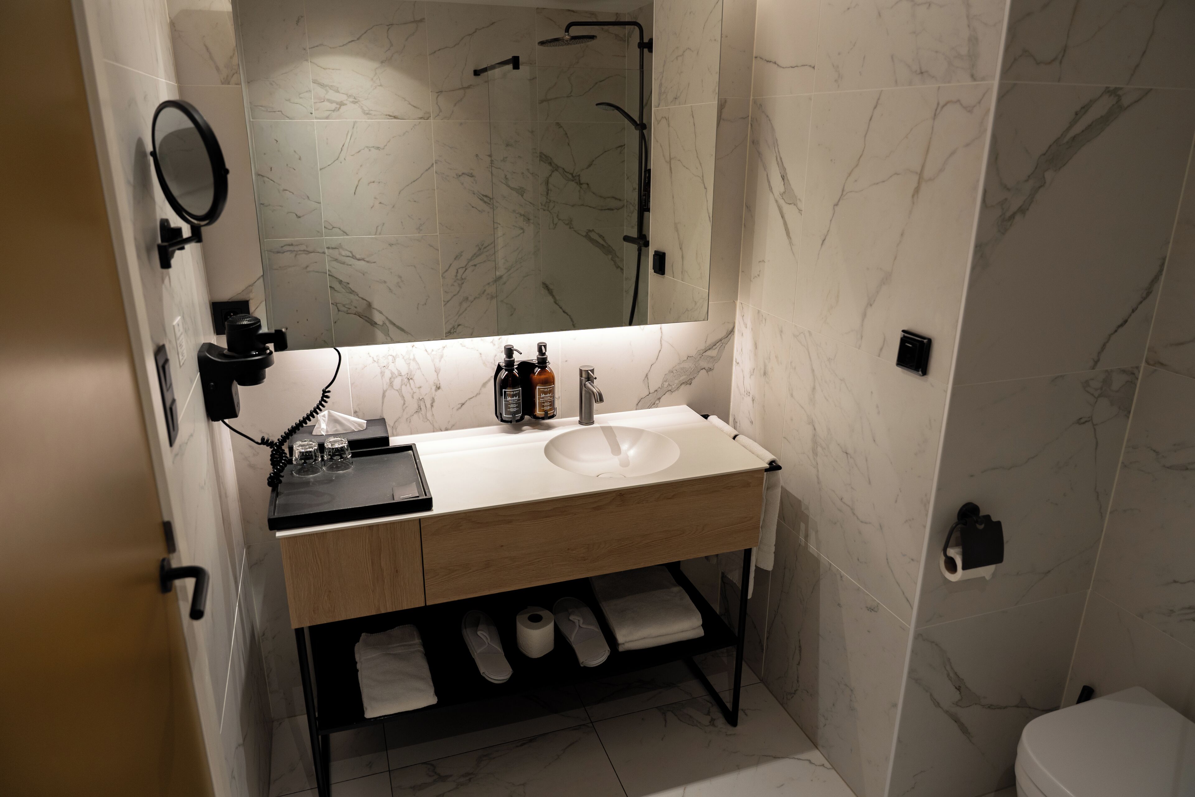 Een moderne badkamer met een marmeren wastafel, een spiegel, een handdouche en een toilet.