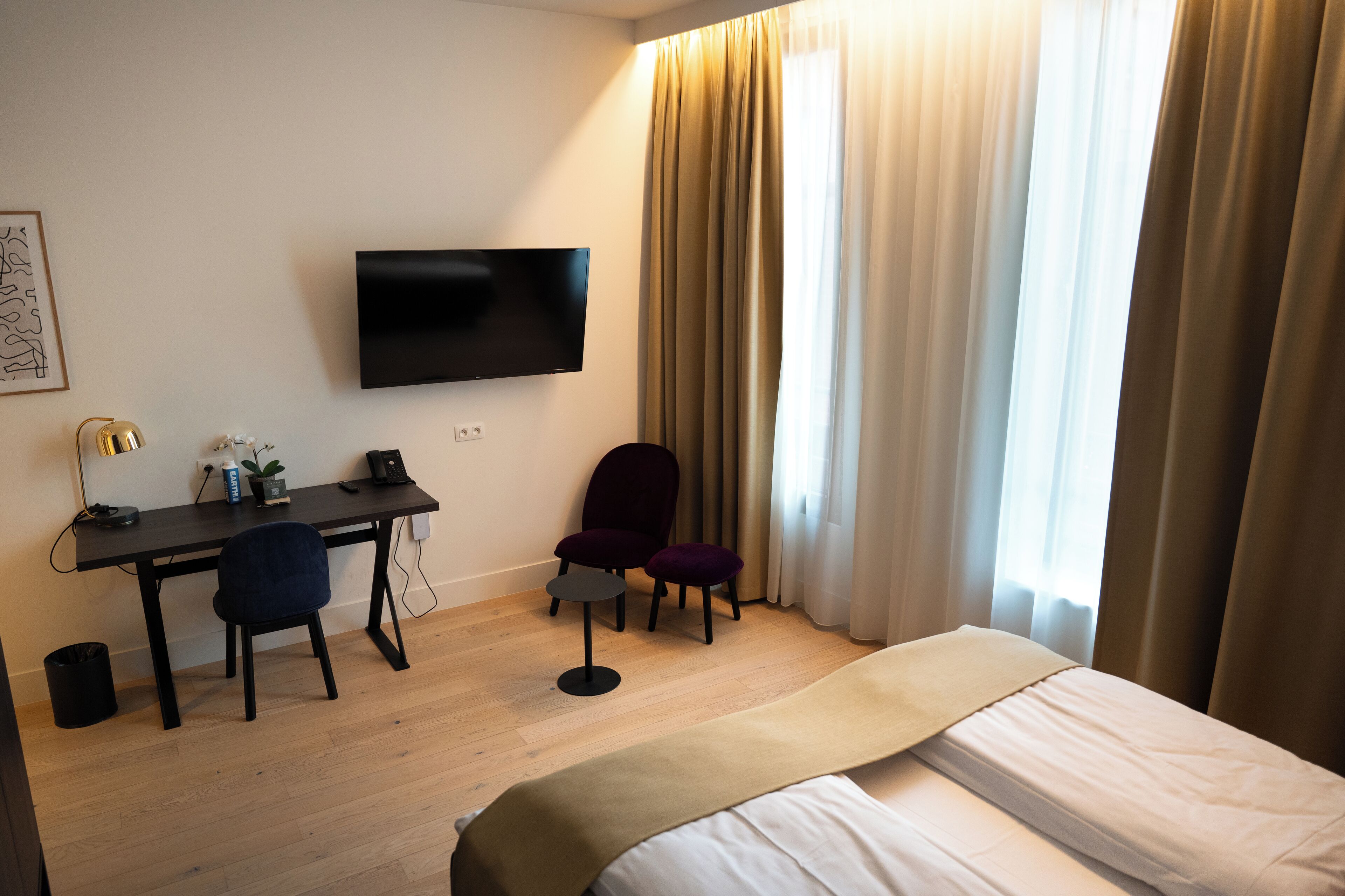 A hotel room with a bed, a desk with two chairs, a television, and a window with curtains.