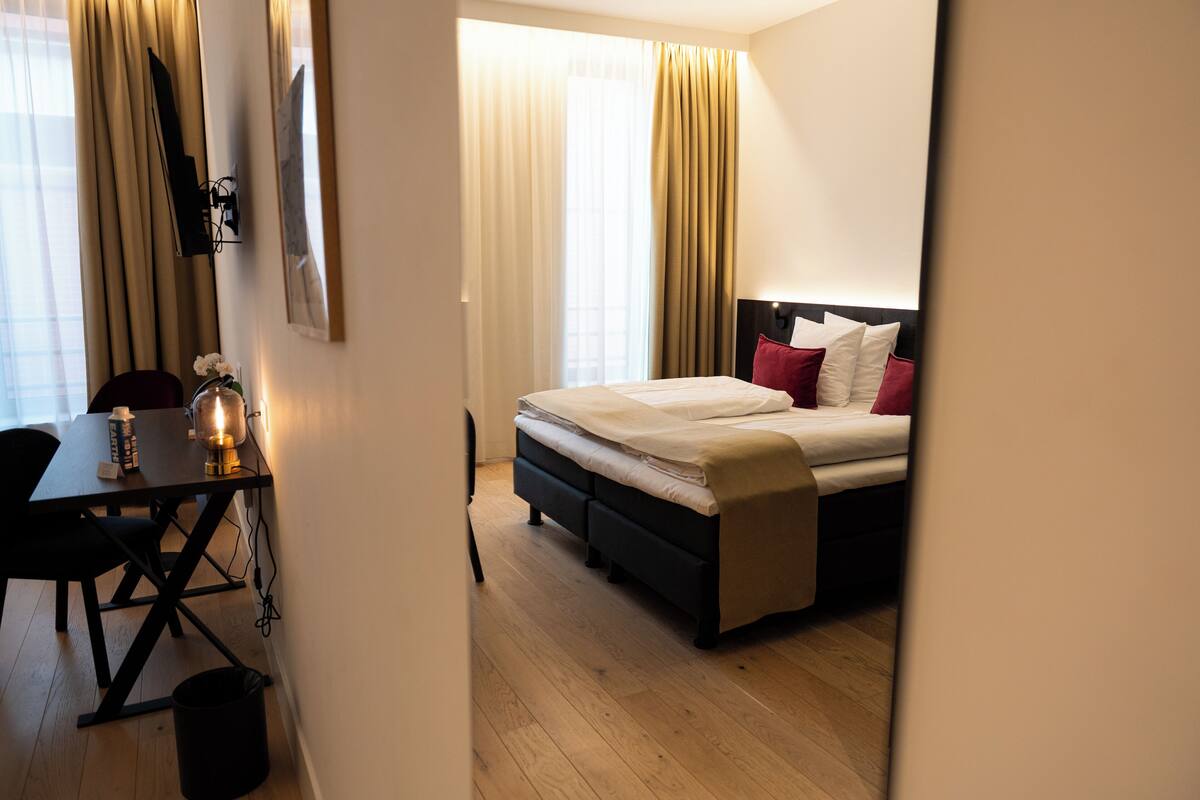 A hotel room with a bed, bedside table, lamp, and curtains.