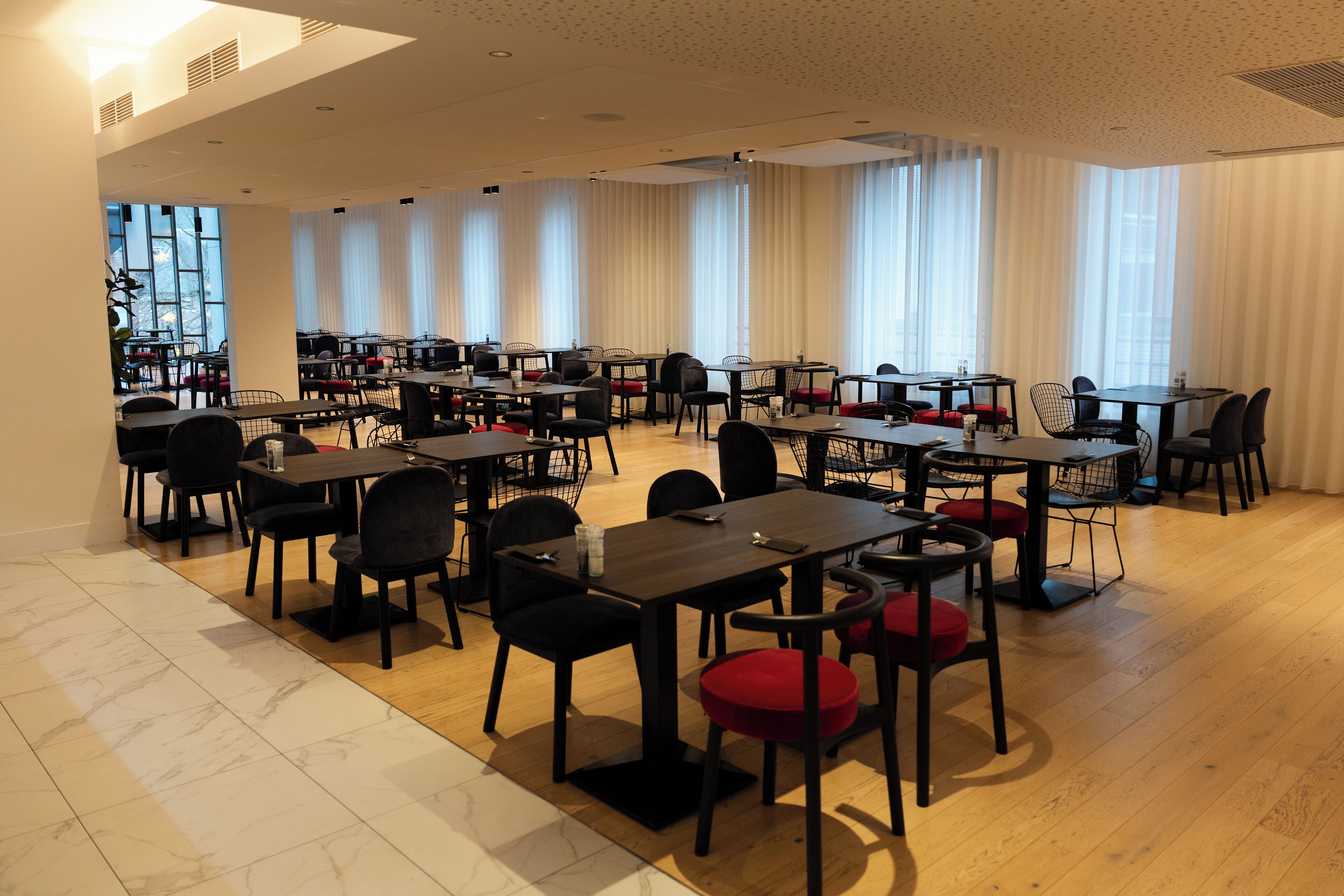 Un amplio comedor con varias mesas y sillas, ventanas grandes con cortinas y un diseño de interiores moderno.