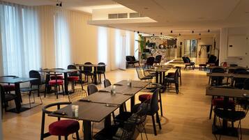 A spacious dining area with multiple tables and chairs, large windows with sheer curtains, and a modern interior design.