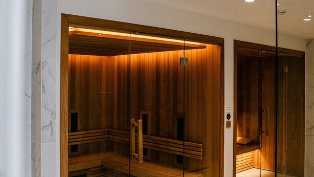 Ein moderner Wellnessraum mit Holzvertäfelung, einer Glastrennwand und Marmorböden.