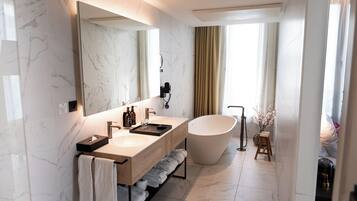 Un baño moderno con paredes de mármol, un espejo grande, una bañera independiente y un tocador con toallero.