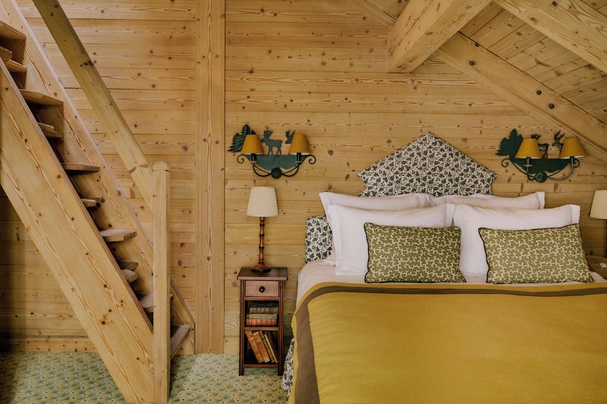 A wooden room with a bed, a nightstand, a lamp, and a bookshelf.