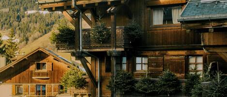A traditional wooden hotel with a balcony, a sign reading "Hotel Saint-Georges," and a view of a mountain in the background.