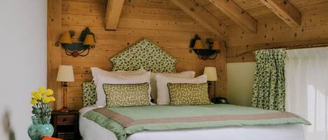 A cozy bedroom with a wooden ceiling, a bed with floral bedding, a nightstand with a lamp, and a chair.