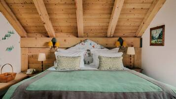 A wooden ceiling with exposed beams, a bed with green bedding, two wall-mounted lamps, and a painting on the wall.