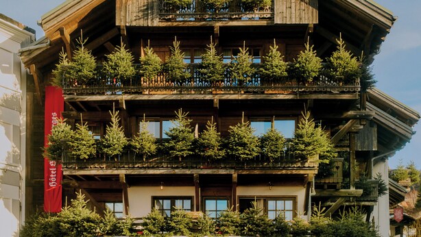 Un hotel de varios pisos con balcones, fachada de madera y un estandarte rojo.