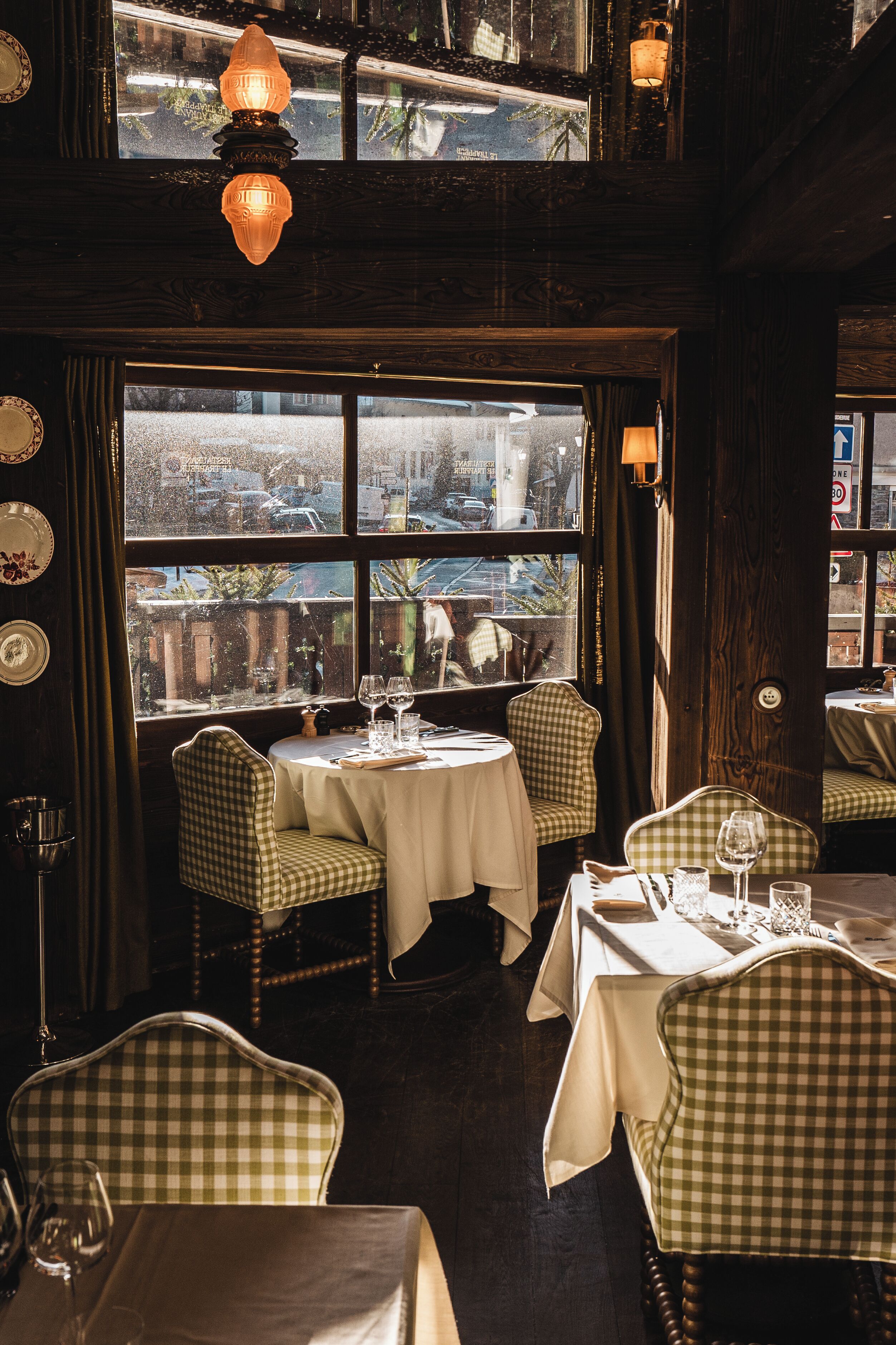 Un restaurante con sillas a cuadros, mesas redondas y vistas de la ciudad a través de amplios ventanales.