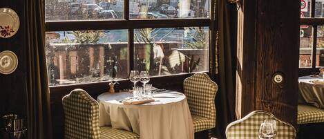 A restaurant with checkered chairs, round tables, and a view of the city through large windows.