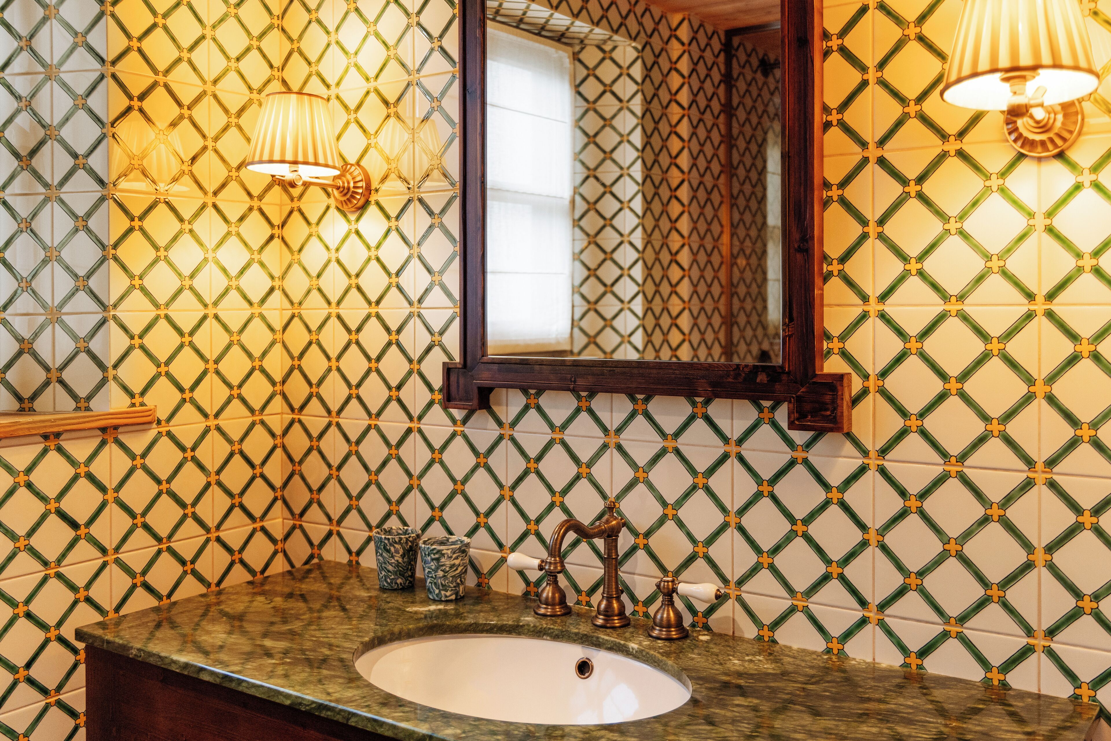 A bathroom with a patterned tile backsplash, a sink with a wooden vanity, and wall-mounted lighting.