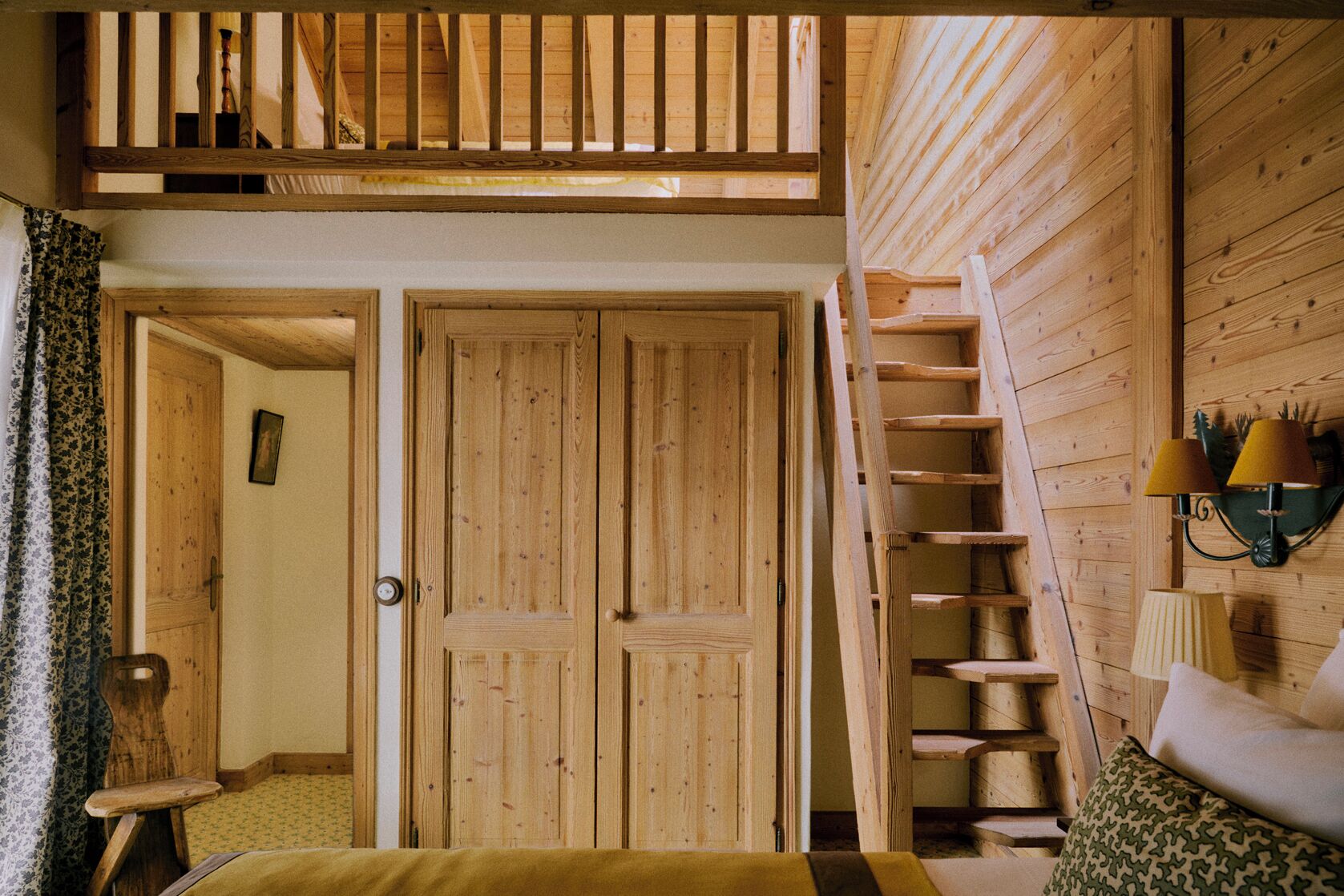 A wooden interior with a loft bedroom, a staircase, and a bed with a patterned pillow.