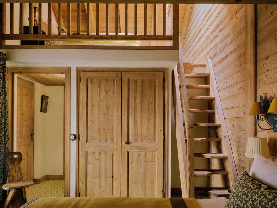 A wooden interior with a loft bedroom, a staircase, and a bed with a patterned pillow.