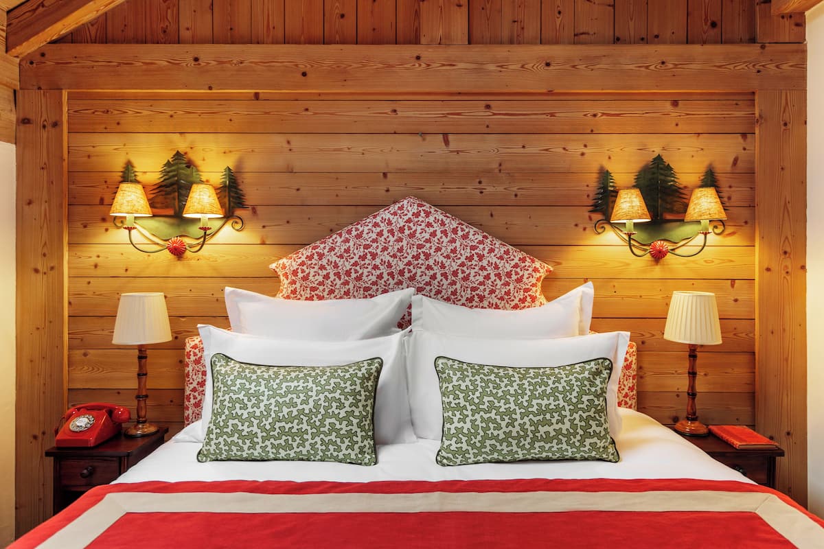 A wooden-paneled room with a bed, two wall-mounted lamps, and a telephone on a nightstand.