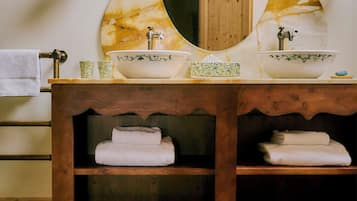 Un baño con tocador de madera, dos lavamanos, un espejo grande y suelo de baldosas.