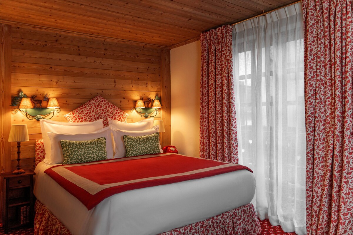 A wooden-paneled bedroom with a bed, floral curtains, and wall-mounted lamps.