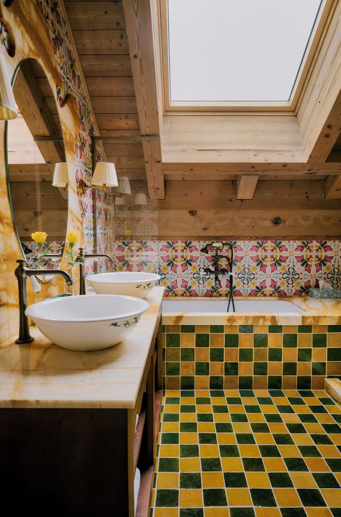 Un baño con tragaluz, vigas de madera, piso de baldosas y un salpicadero con motivos florales.