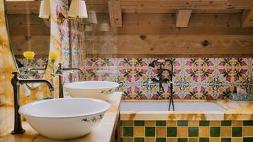 Un baño con tragaluz, vigas de madera, piso de baldosas y un salpicadero con motivos florales.