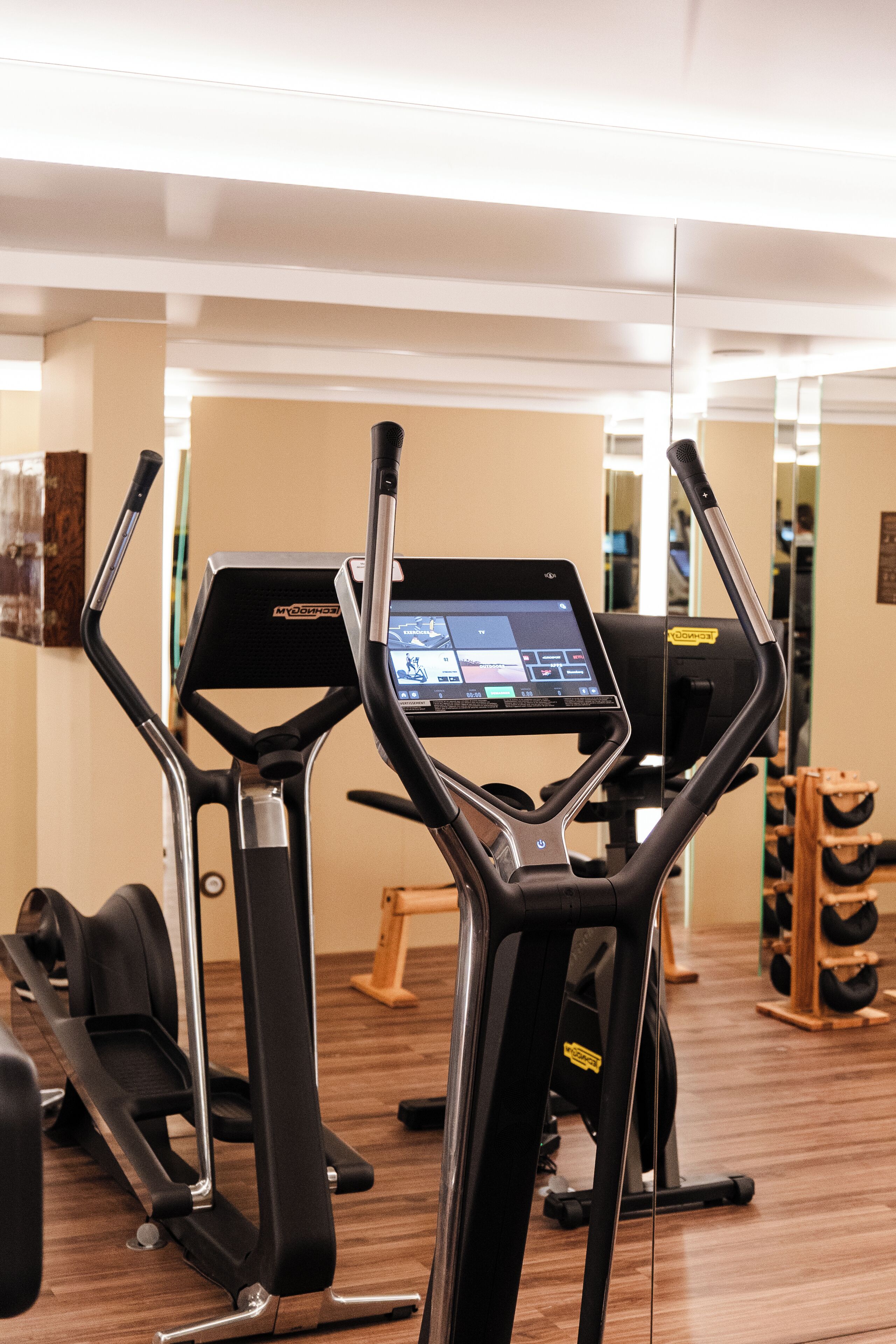 Une salle de sport équipée de tapis de course, d’appareils d’exercice et d’un mur recouvert de miroirs.